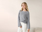 Une femme portant un pull gris et un pantalon blanc.