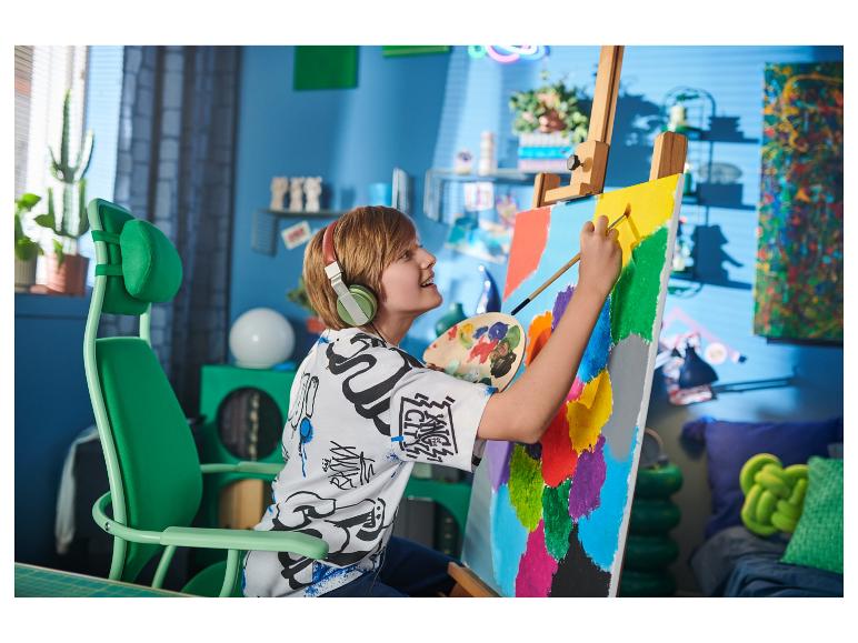 Garçon blond avec un casque peignant sur toile dans une chaise verte.