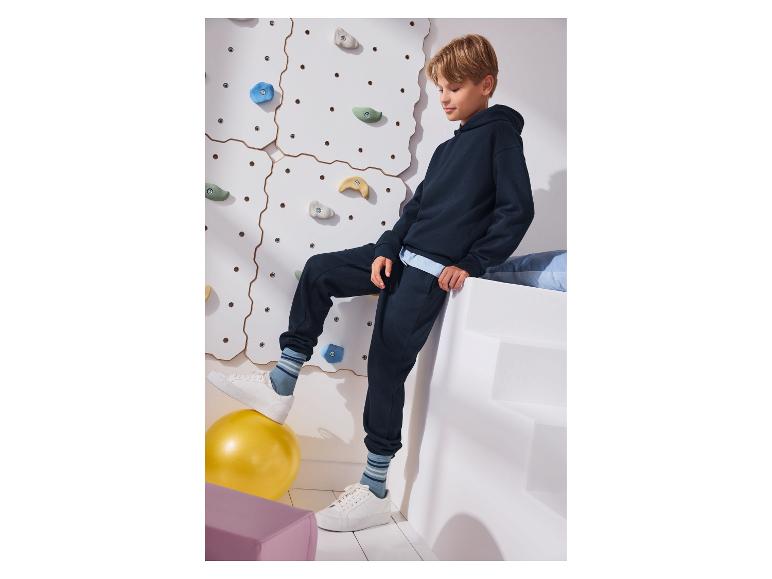 Garçon en sweat à capuche et pantalon de survêtement bleu marine, un pied sur un ballon jaune.