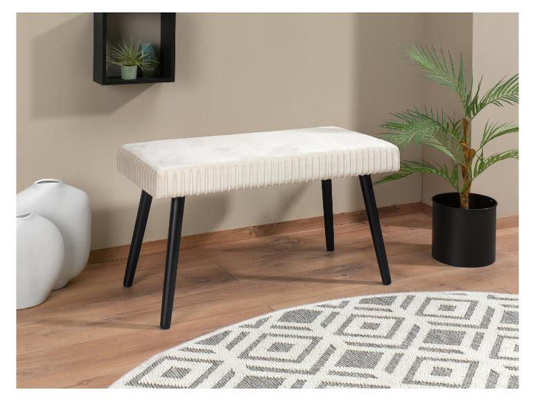 Un banc de couleur crème avec des pieds noirs sur un tapis à motif géométrique gris et blanc.