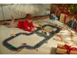 Fille joue avec piste de voitures et train en bois, cadeaux de Noël en arrière-plan.
