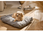 Un petit chien couché sur un panier pour chien gris sur le sol de la maison.