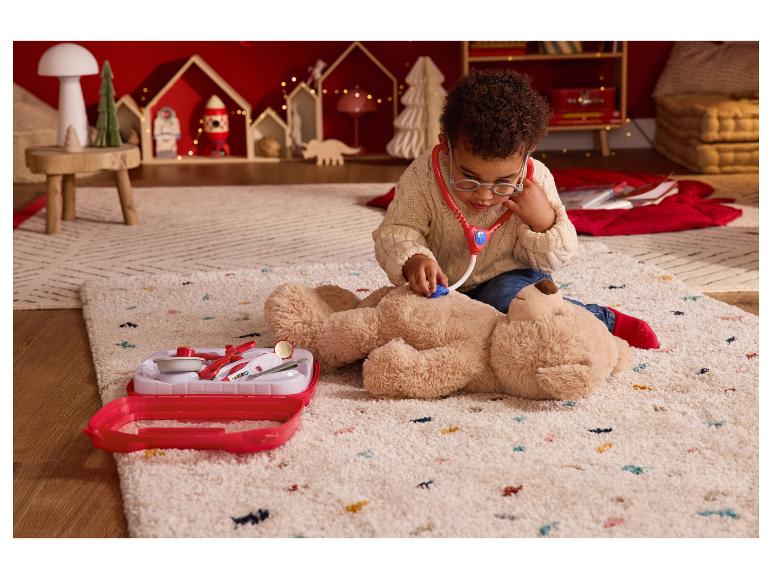Un enfant joue au docteur avec un ours en peluche et une trousse médicale jouet sur un tapis.