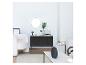 Commode noire, miroir rond, fauteuil blanc et tourne-disque dans un salon.