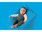 Bébé heureux en barboteuse tricotée verte assis sur un pouf bleu moelleux.