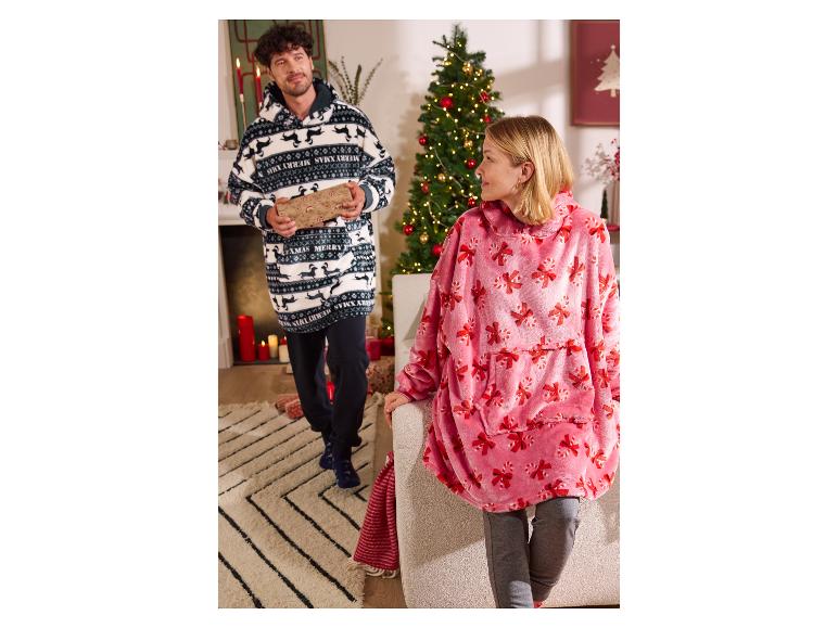 Deux personnes portent des couvertures surdimensionnées sur le thème de Noël, l'une tenant un cadeau.