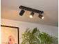 Barre de spots de plafond noire avec trois lumières réglables éclairant une plante et une œuvre d'art.