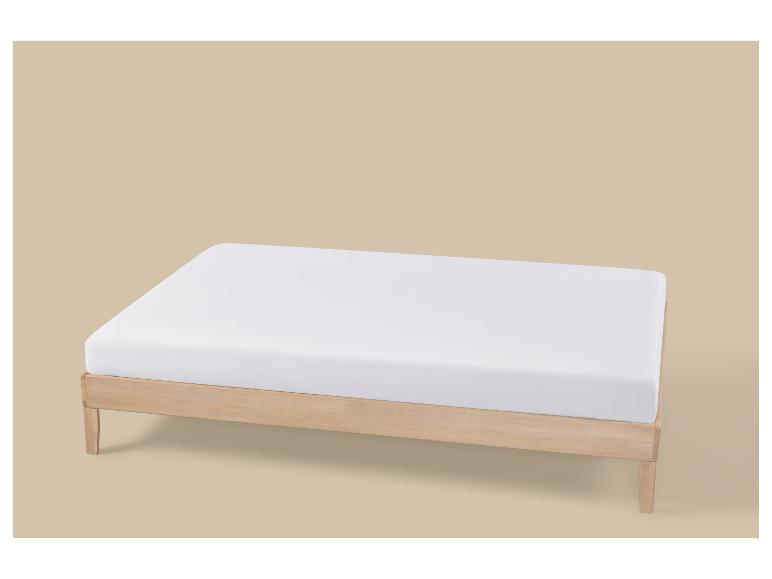 Un cadre de lit en bois clair avec un matelas blanc sur fond beige.