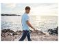 Un homme portant un polo bleu et un jean marche au bord de la mer.