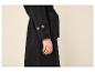 Manteau noir avec des boutons marron sur les manches et une bague dorée au doigt.