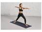 Une femme en brassière de sport noire et leggings fait du yoga sur un tapis bleu Decathlon.