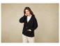 Une femme porte un pull noir et un pantalon beige.