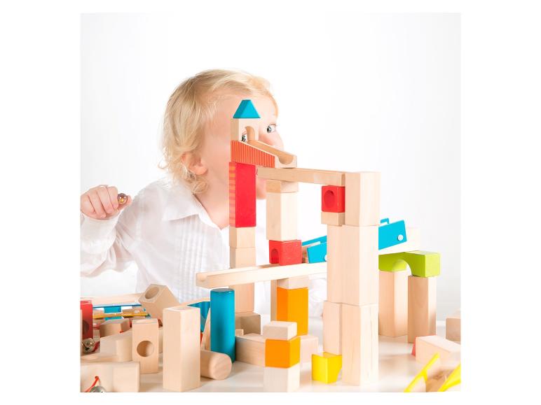 Enfant jouant avec des blocs de construction en bois et un circuit de billes.