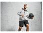 Homme en sweat-shirt gris et short noir, tenant un ballon d'entraînement noir.