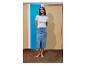 Femme en t-shirt blanc côtelé et jupe midi en jean, pieds nus sur le sable.