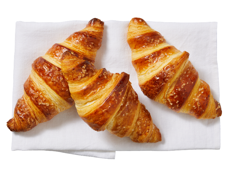 Trois croissants dorés et croustillants, saupoudrés de sucre, sur une serviette blanche.