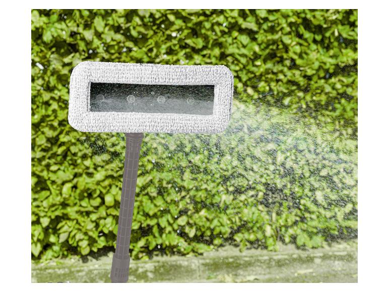 Pulvérisateur de jardin avec jet d'eau sur fond de haie verte.