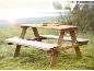 Table de pique-nique en bois pour enfants avec coussins et nourriture jouet dans un jardin.