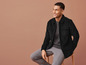 Un homme portant une veste en velours côtelé noire et un pantalon gris.