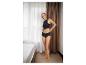 Femme en sous-vêtements noirs, ajustant son slip, dans une chambre lumineuse.