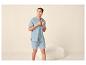 Homme souriant en pyjama d'été bleu clair, chemise à manches courtes et short.