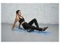 Une femme utilise un rouleau en mousse pour la libération myofasciale sur un tapis de yoga.