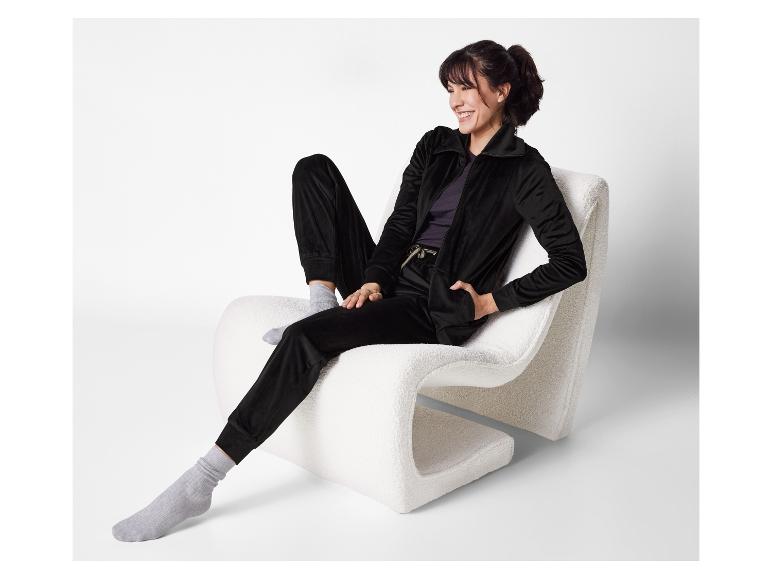 Femme relaxée sur un fauteuil blanc avec un ensemble en velours noir.