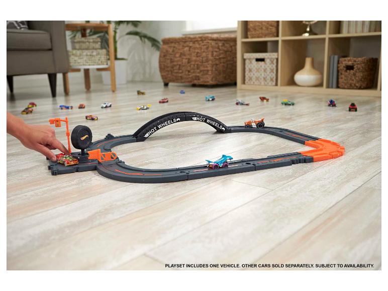 Piste de course Hot Wheels avec plusieurs petites voitures sur un parquet.