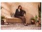 Femme en cardigan tricoté et pantalon marron, assise sur un banc avec plantes et sac.