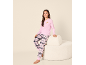 Fille en haut rose à manches longues avec motif croissant et pantalon de pyjama à carreaux roses, assise sur un tabouret crème.