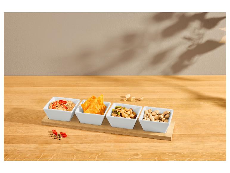 Plateau en bambou avec quatre bols en céramique remplis de trempettes, nachos et noix.