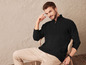 Un homme porte un pull noir et un pantalon beige.
