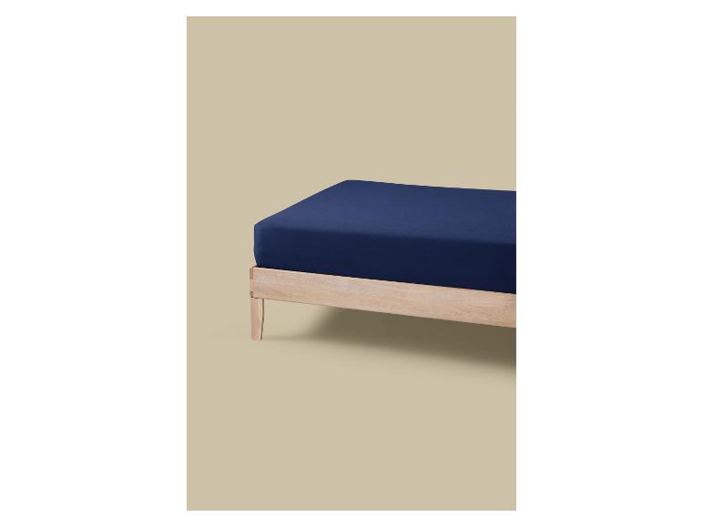 Un matelas bleu foncé sur un cadre en bois clair sur fond beige.