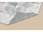 Tapis gris et blanc à motifs avec un coin relevé, révélant le dessous antidérapant.
