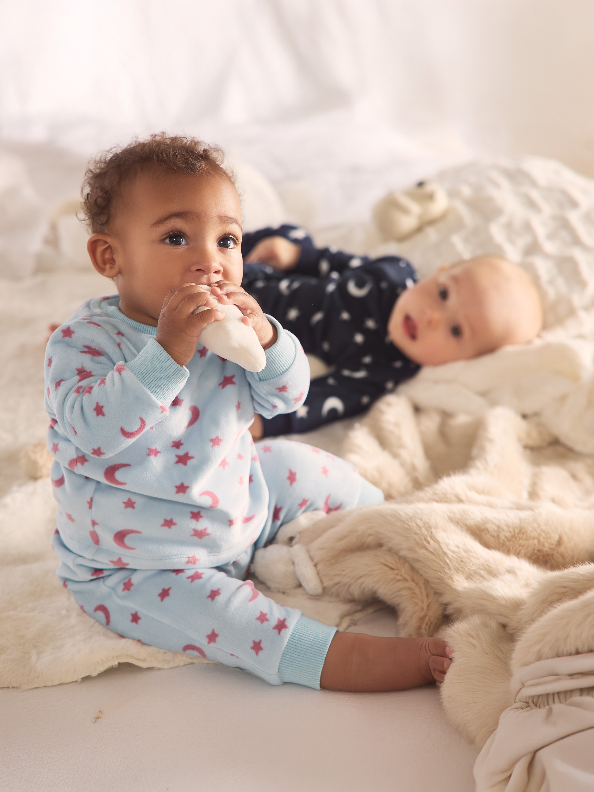Deux bébés en pyjama étoiles et lunes, l'un assis, l'autre allongé sur une couverture douce.