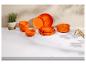 Service de table orange avec assiettes et bols, une plante en pot et des couverts sur un comptoir blanc.