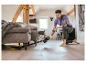 Homme nettoyant sous un canapé avec un aspirateur balai sans fil sur un parquet.