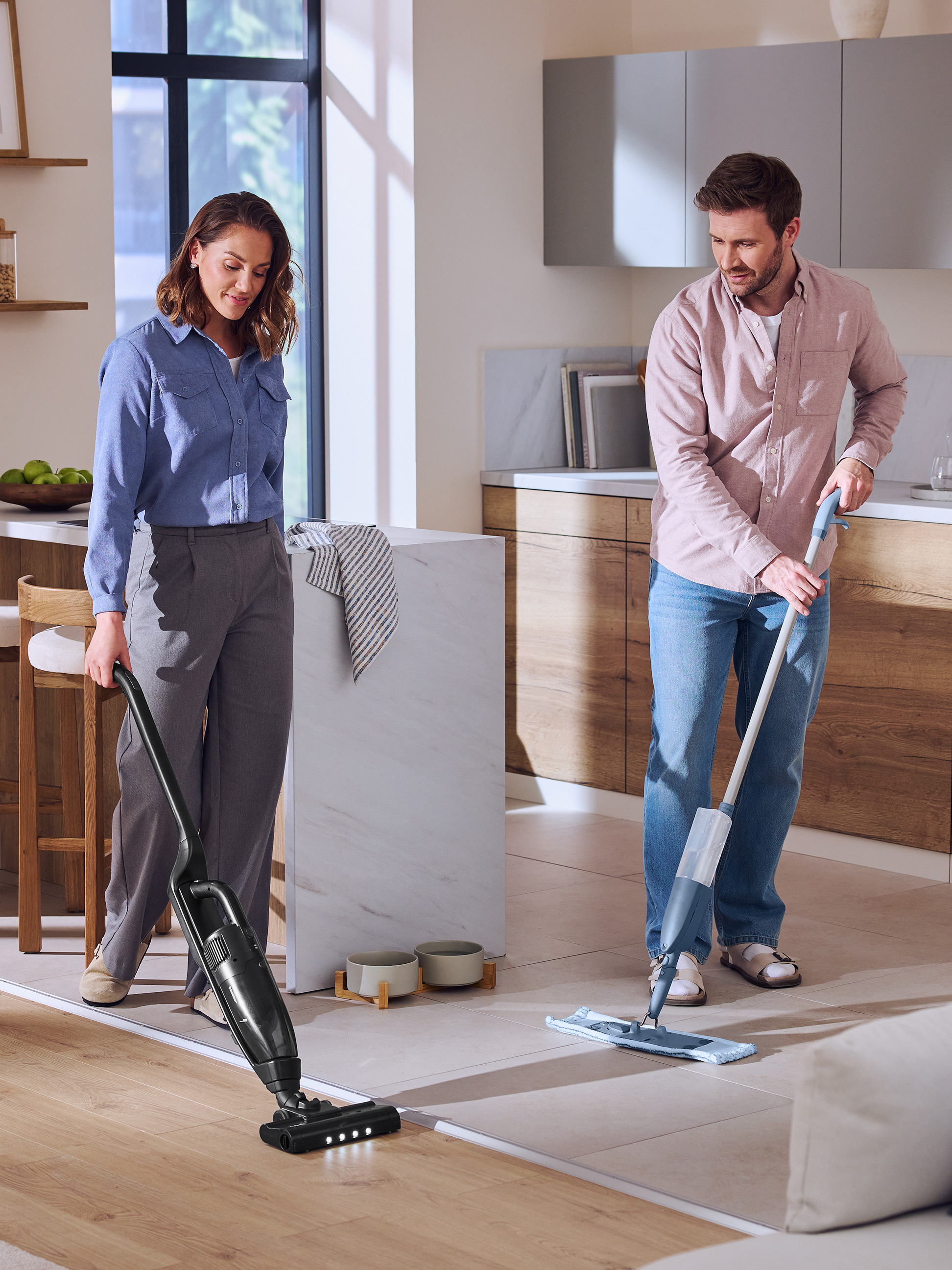 Un couple nettoie le sol de la cuisine avec un aspirateur balai et une serpillière.