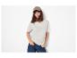 Femme en t-shirt beige, jean bleu et casquette marron, mains dans les poches.