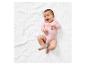 Bébé dans un body rose allongé sur une couverture blanche.