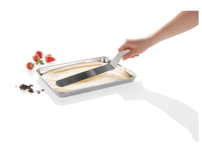 Une main utilise une spatule pour étaler une pâte à gâteau dans un moule.