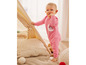 Un bébé dans un pyjama rose avec un motif de lune et d'étoiles se tient dans une tente avec des coussins.