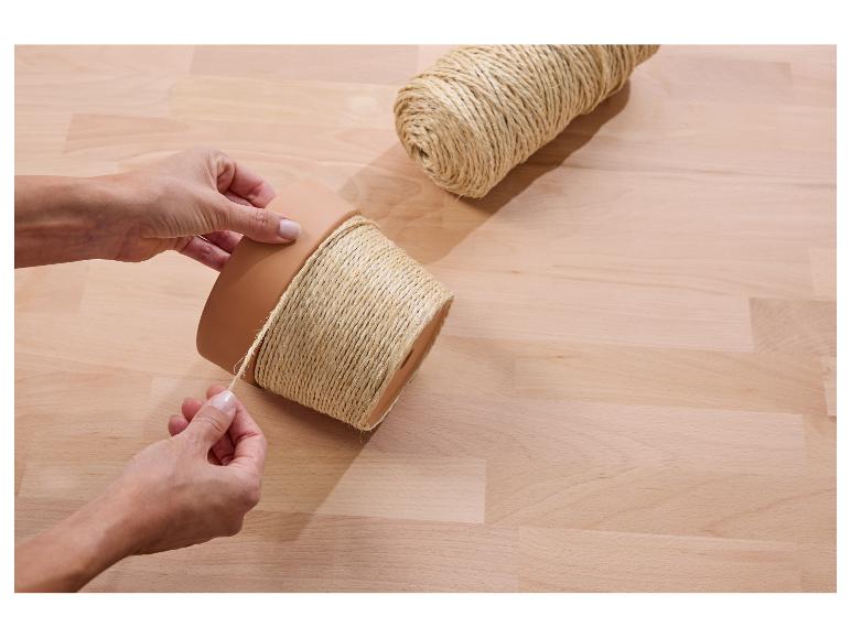 Mains enroulant de la ficelle autour d'un pot sur une table en bois, avec une bobine de ficelle à côté.