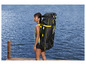 Une femme avec un sac noir pour un paddleboard gonflable au bord de l'eau.