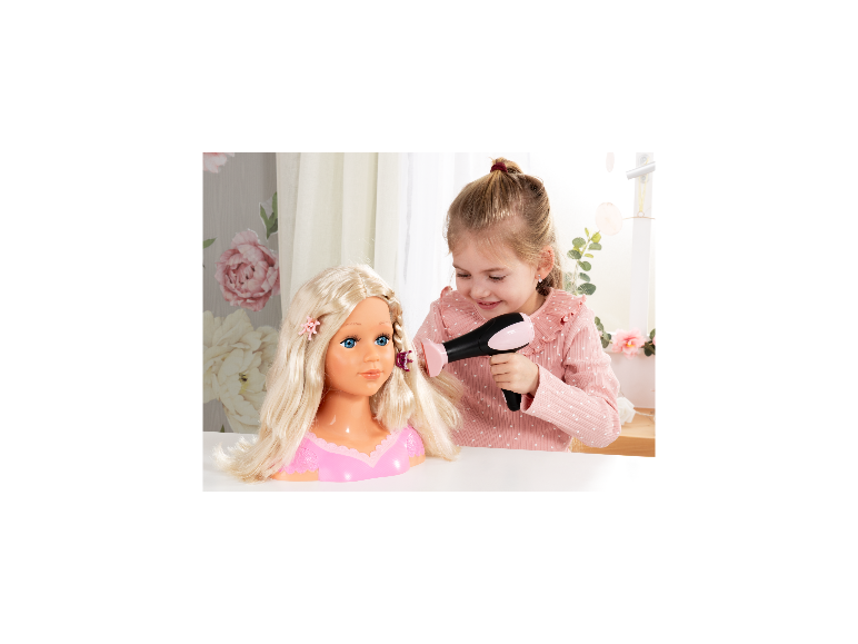 Une jeune fille coiffe la tête à coiffer Charlene de Bayer Design avec un sèche-cheveux jouet.