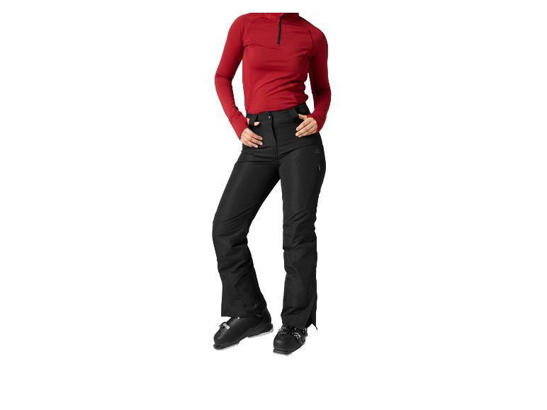 Femme portant un pantalon de ski noir et une couche de base rouge, avec des chaussures de ski.