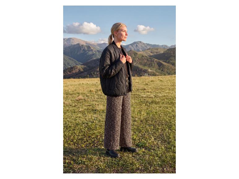 Femme en veste matelassée noire et pantalon imprimé léopard dans un paysage montagneux.