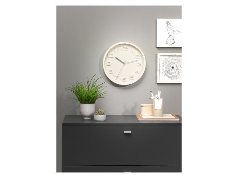 Horloge murale blanche, plantes, et commode grise dans un décor minimaliste.