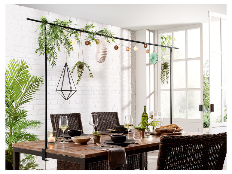 Une table à manger avec des chaises en rotin et une étagère décorative avec des plantes suspendues et des lumières.