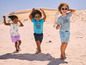 Des enfants sur la plage, portant des vêtements d'été et des lunettes de soleil.
